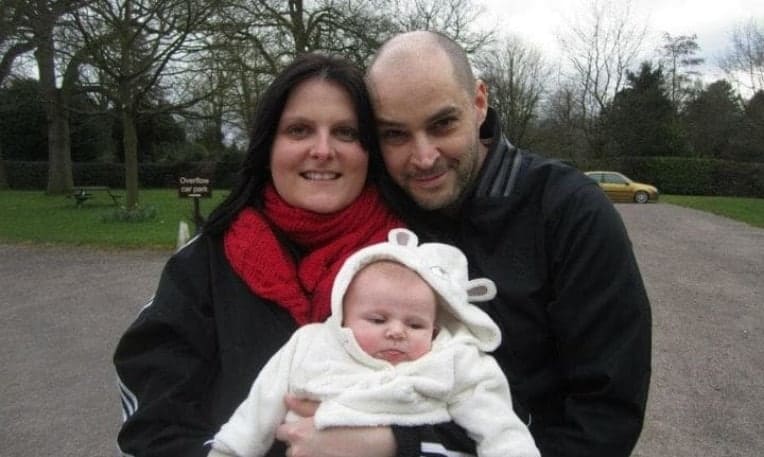 A bebê Millie nos braços de seus pais, Joanne e Dan