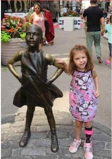 A menina Zoey durante sua luta contra o câncer ao lado da estátua “fearless girl” (garota destemida em inglês)