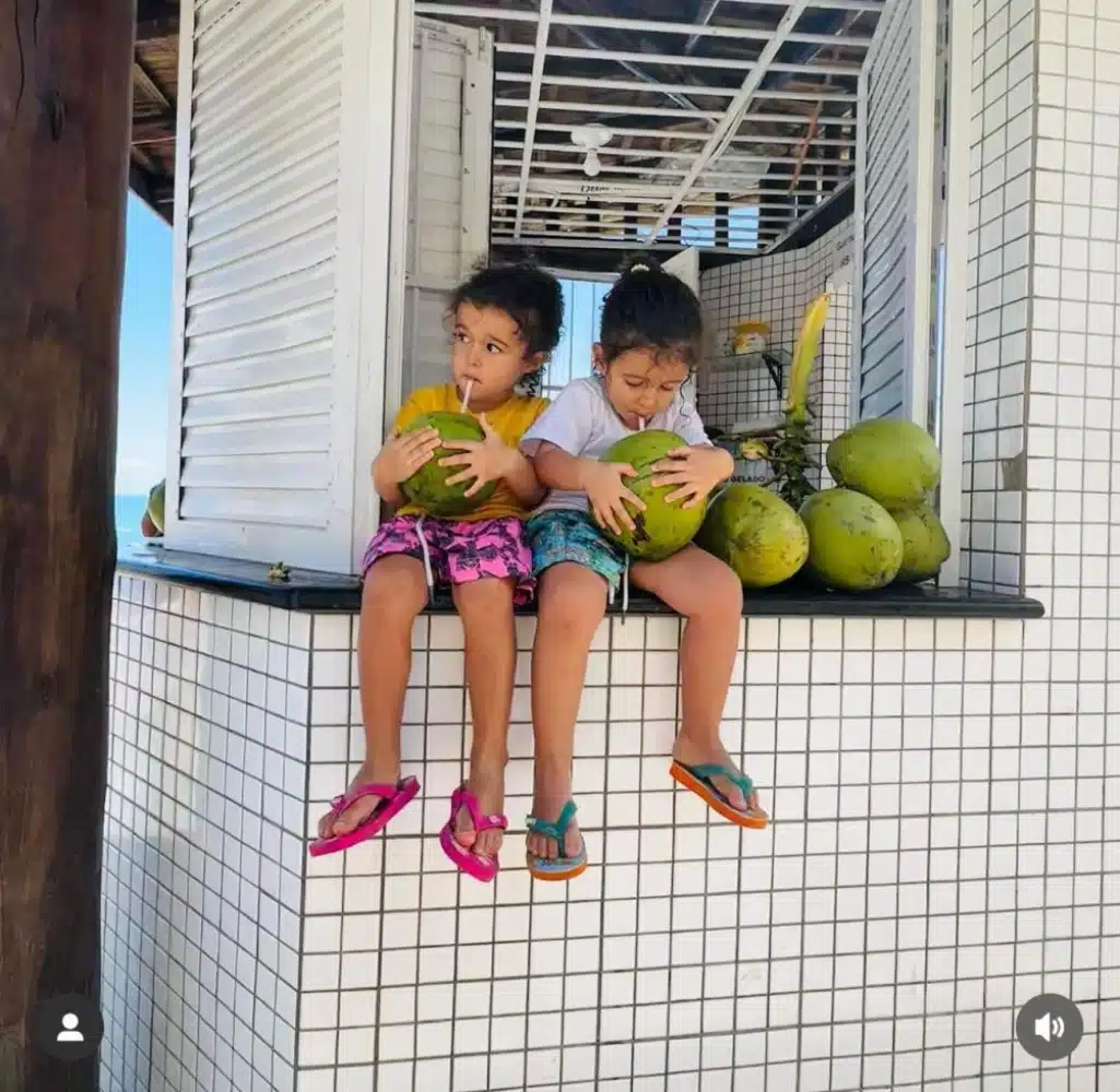 As gêmeas Kim e Tiê, filhas de Nanda Costa, se refrescando com uma água de coco